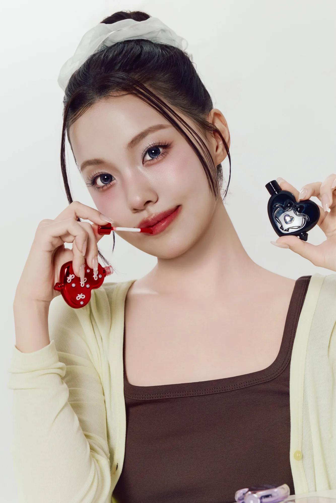 붉은 케이스와 검은 케이스를 든 채 브러시로 입술에 바르는 모습
