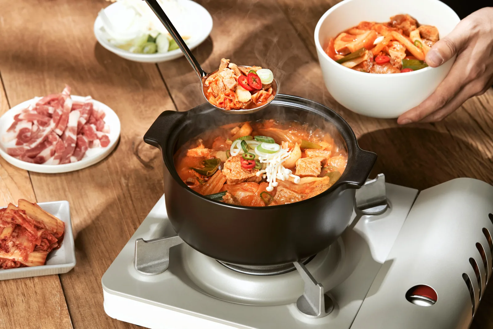 휴대용 화로 위 검은 뚝배기에서 끓는 김치찌개를 국자로 뜨는 모습
